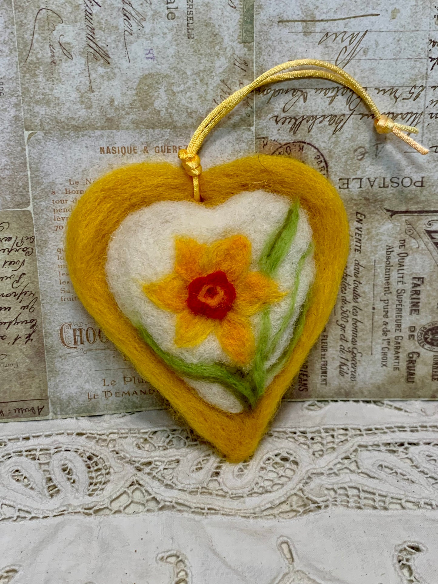 Heart-shaped felted ornament with a daffodil design on a textured background