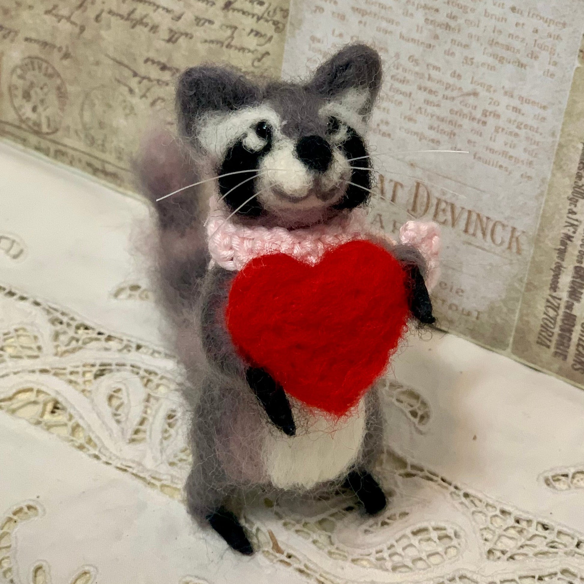 Stuffed raccoon toy holding a red heart against a textured background