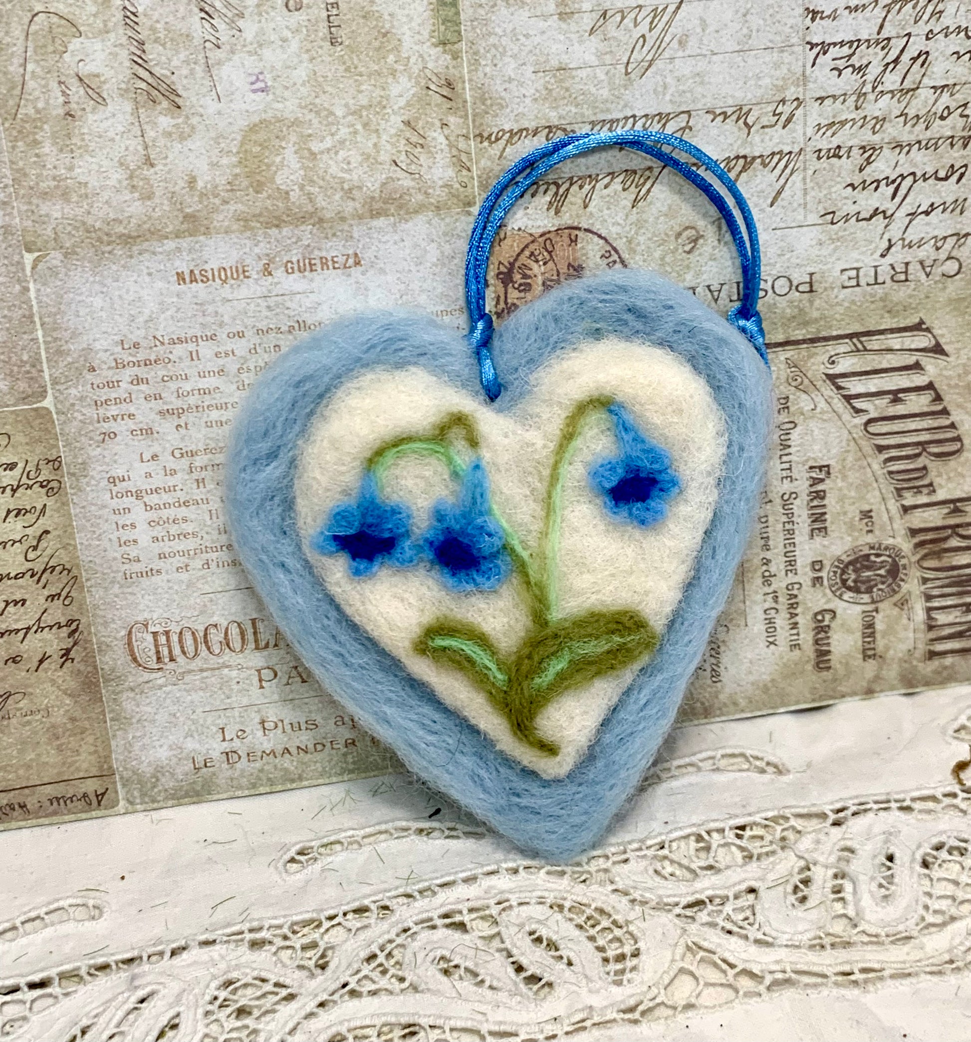 Heart-shaped felted ornament with floral design on a textured background