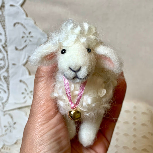 Small white felted sheep toy held in a hand with a lace background