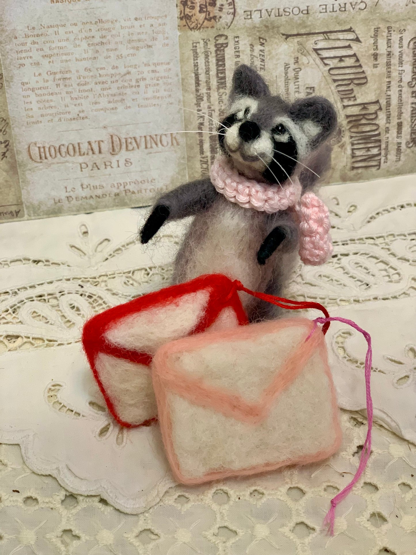 Stuffed raccoon toy with a pink scarf holding two soap bars on a textured surface.