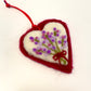 Heart-shaped felt ornament with embroidered flowers and a red ribbon on a white background