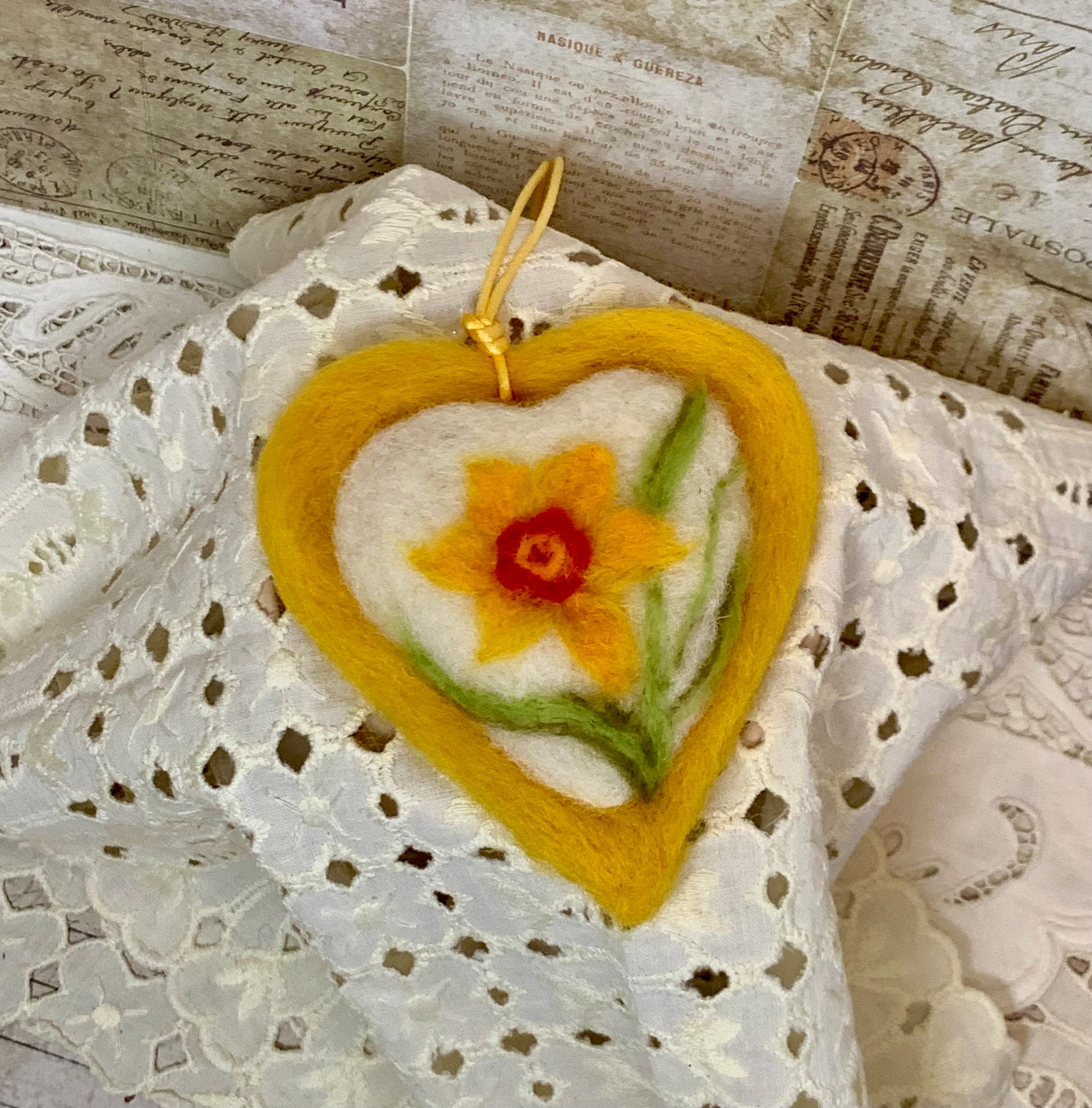 Heart-shaped felted ornament with a yellow flower on a textured surface