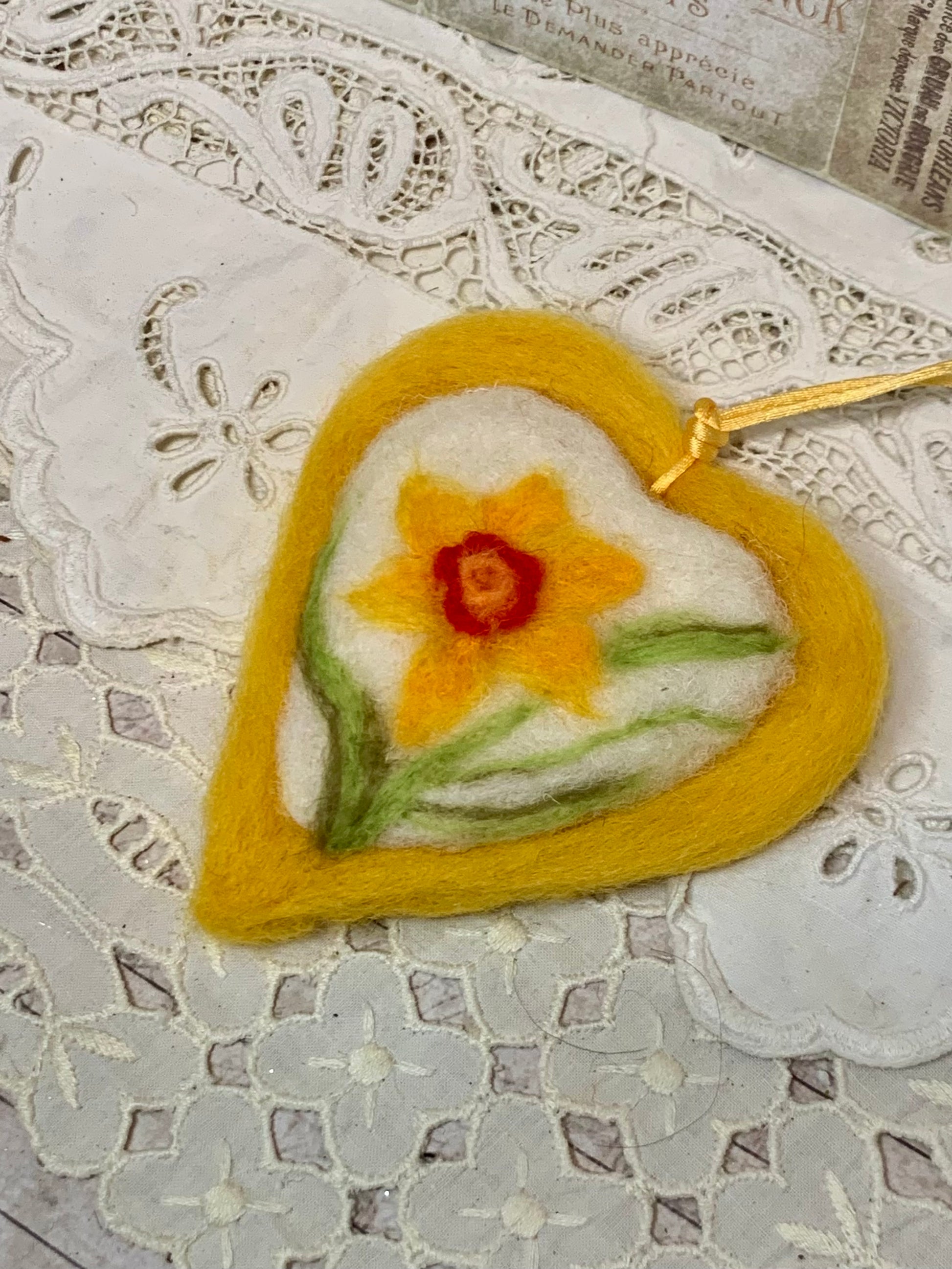 Heart-shaped felted craft with a daffodil design on a lace surface