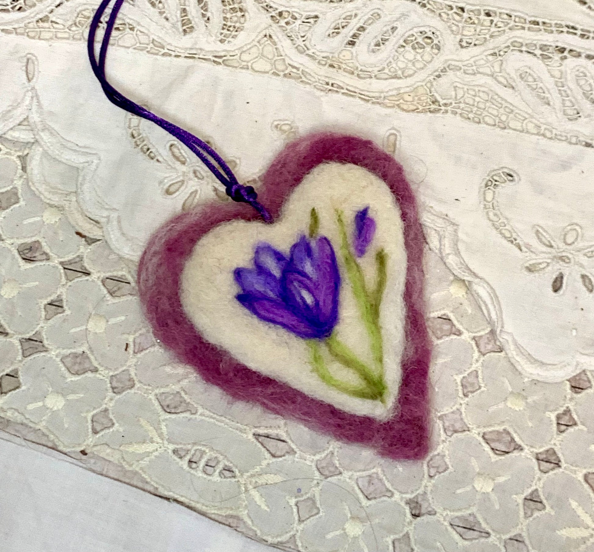 Heart-shaped felted pendant with a purple flower design on a lace background