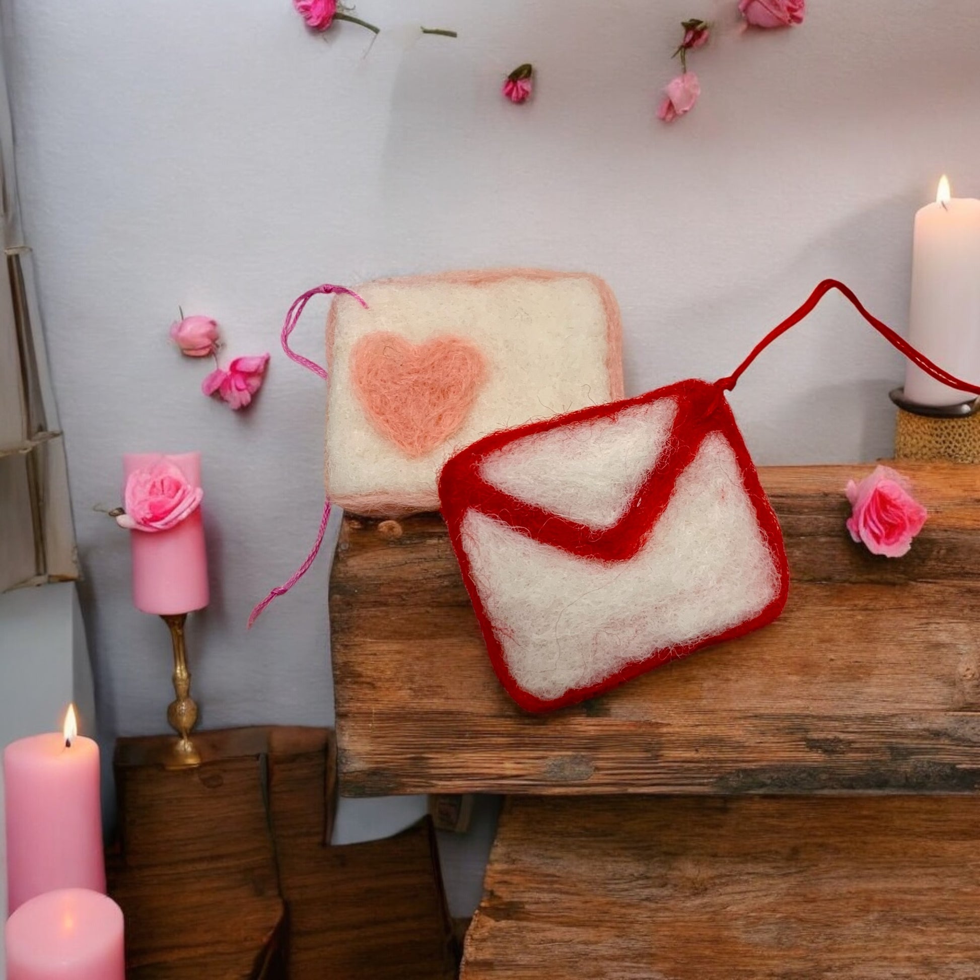 Decorative items including a heart-shaped pink object and a red and white letter-shaped object on a wooden surface with candles and flowers.