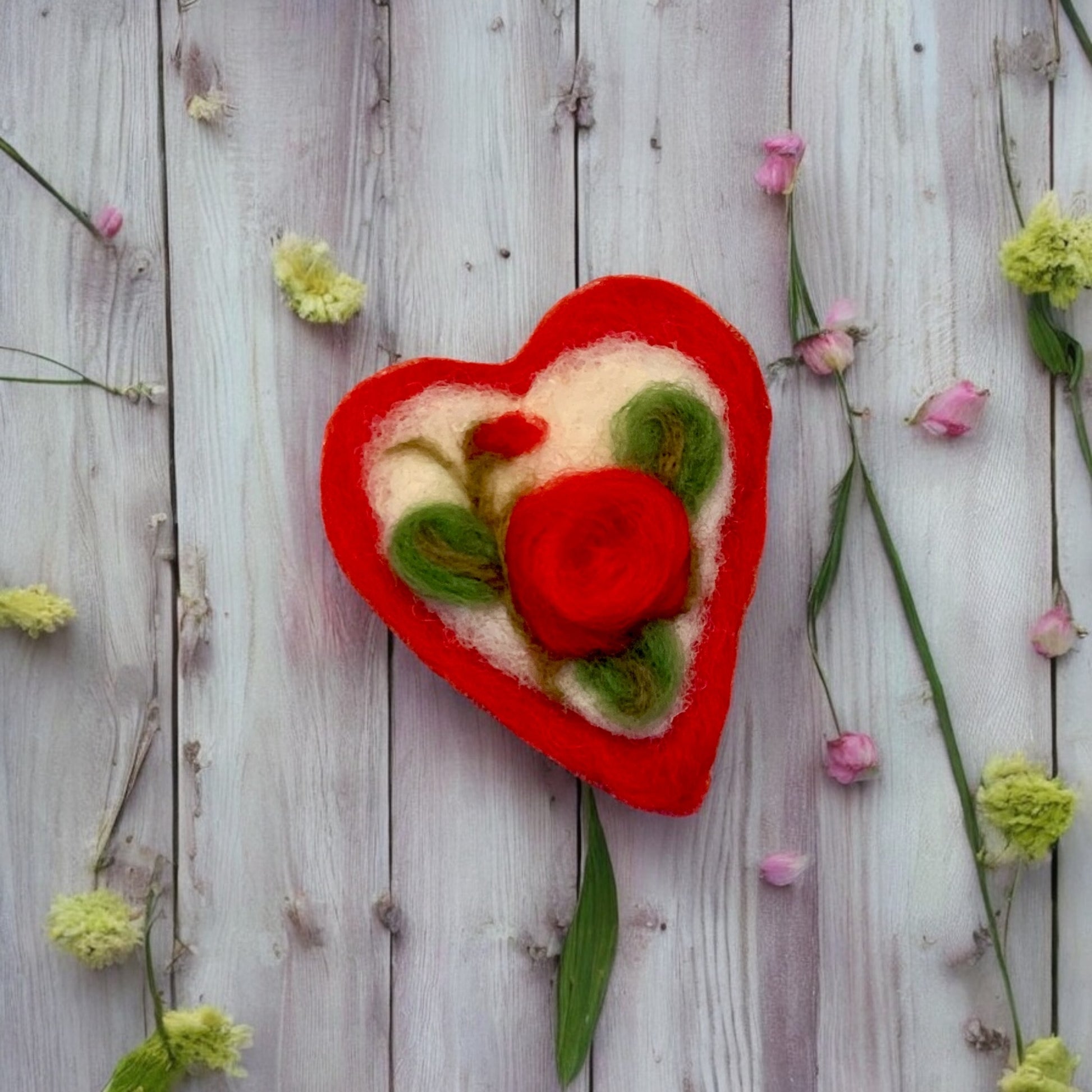 Heart-shaped felted rose on a wooden surface with flowers around