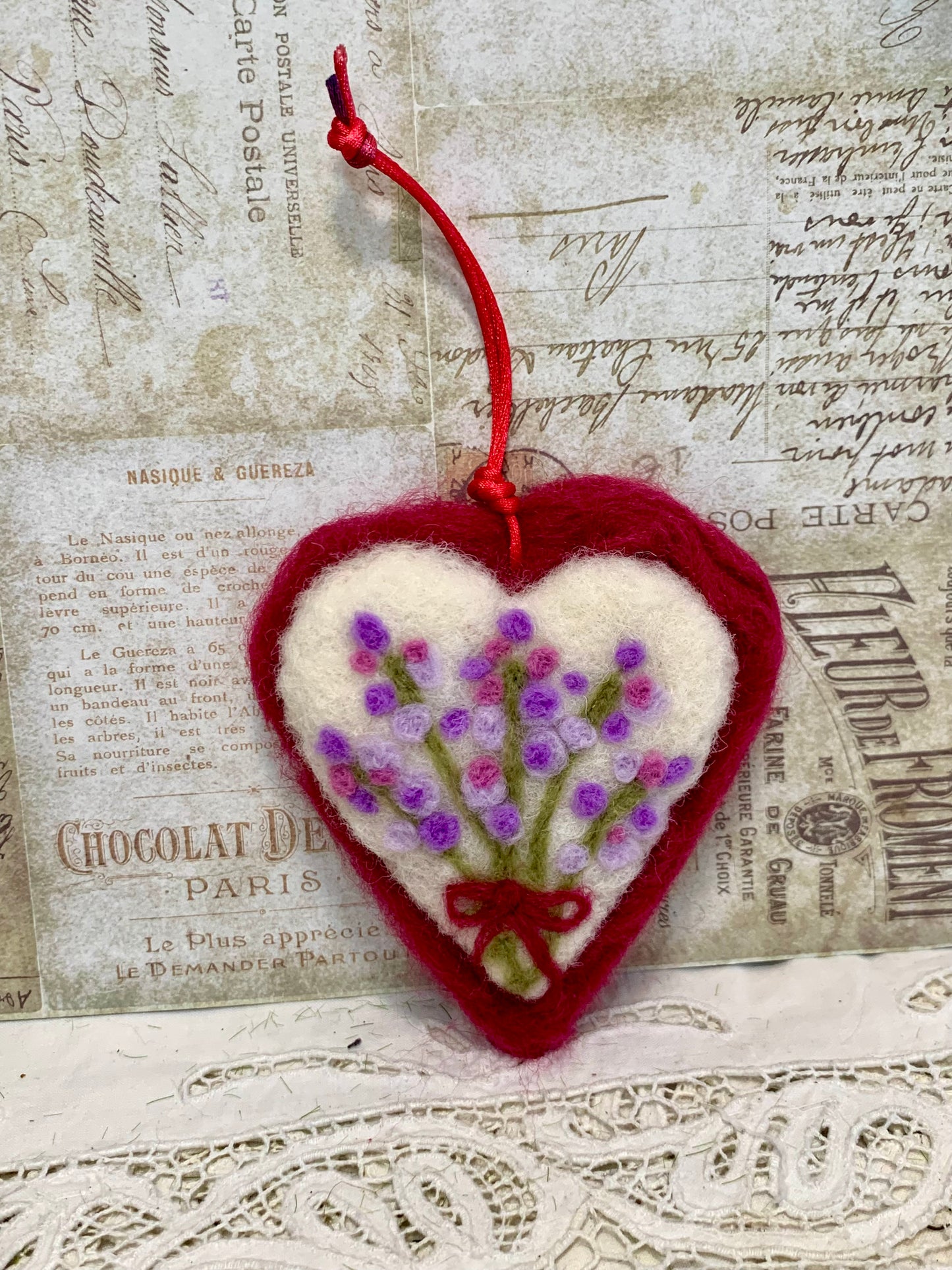 Heart-shaped embroidered ornament with flowers on a textured paper background