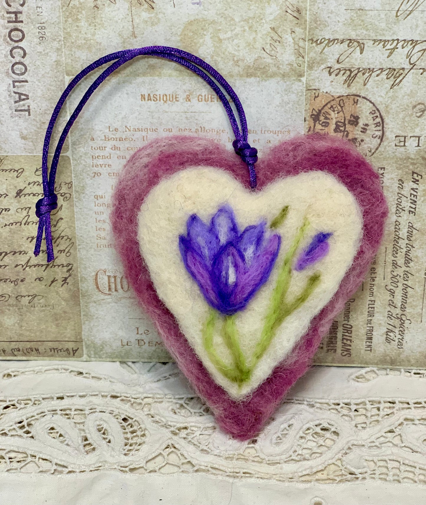 Heart-shaped felted ornament with a purple flower on an old newspaper background