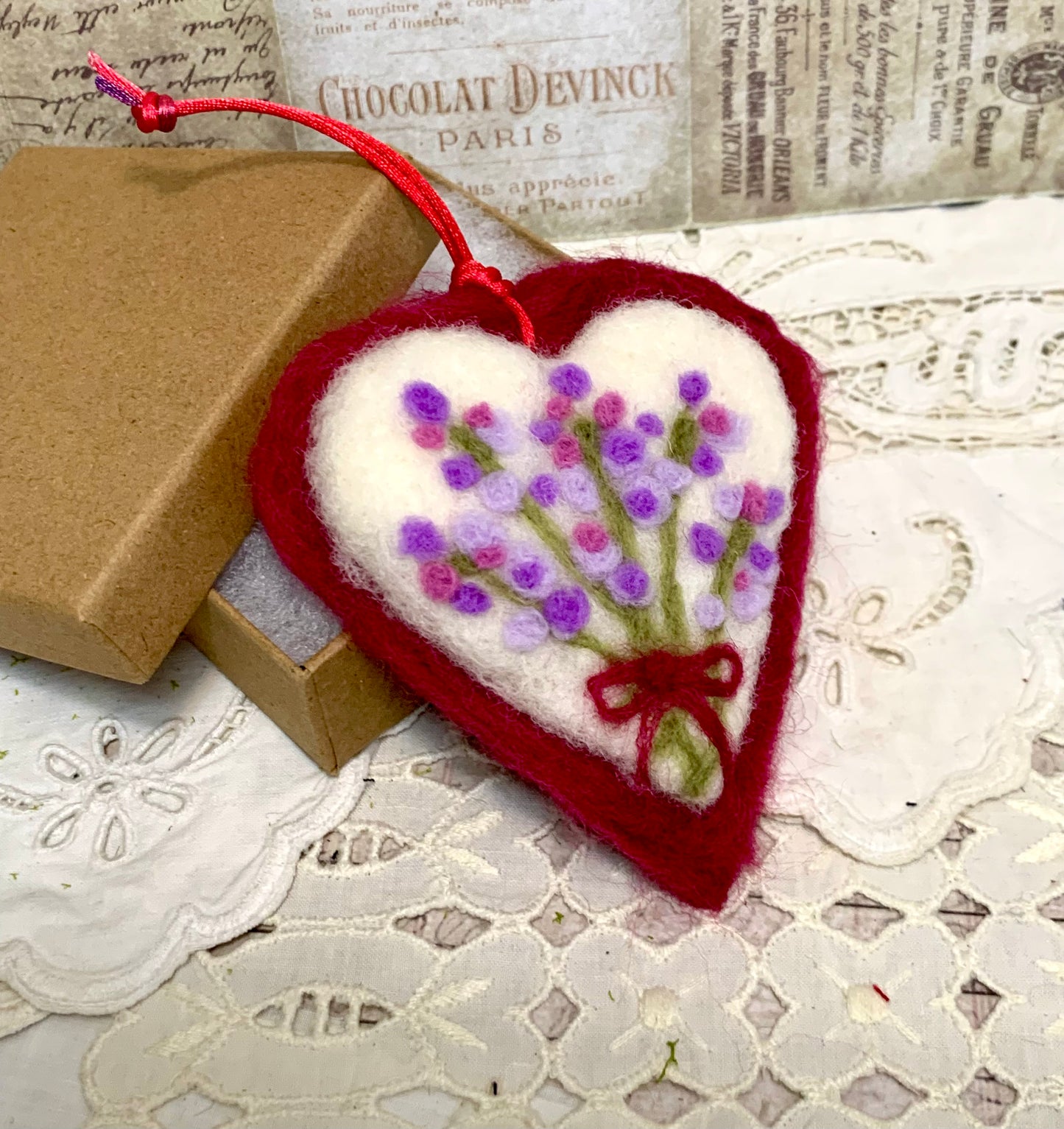Heart-shaped embroidered ornament with lavender design on a lace surface