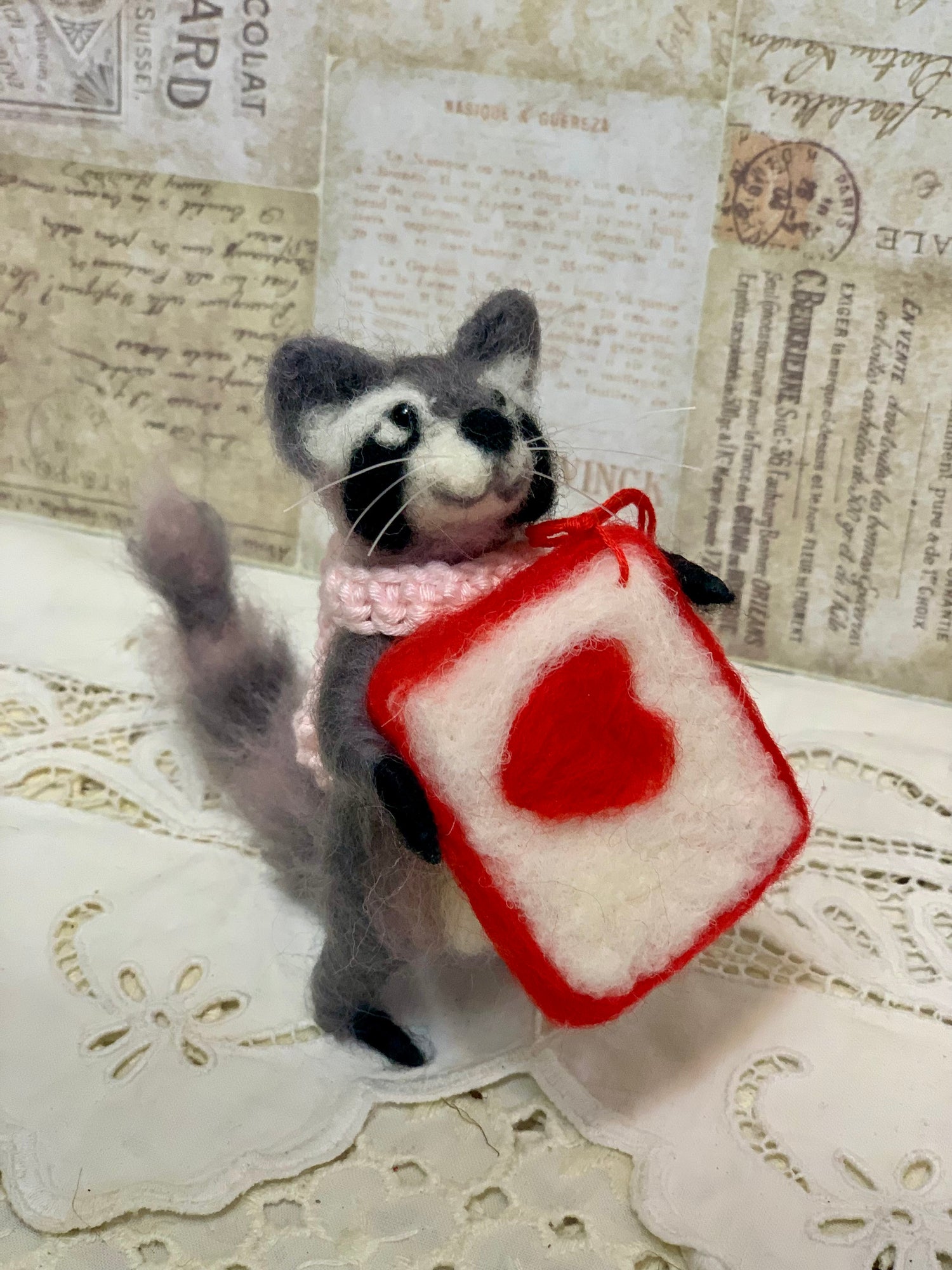 Toy raccoon holding a red and white block with a heart on a textured background