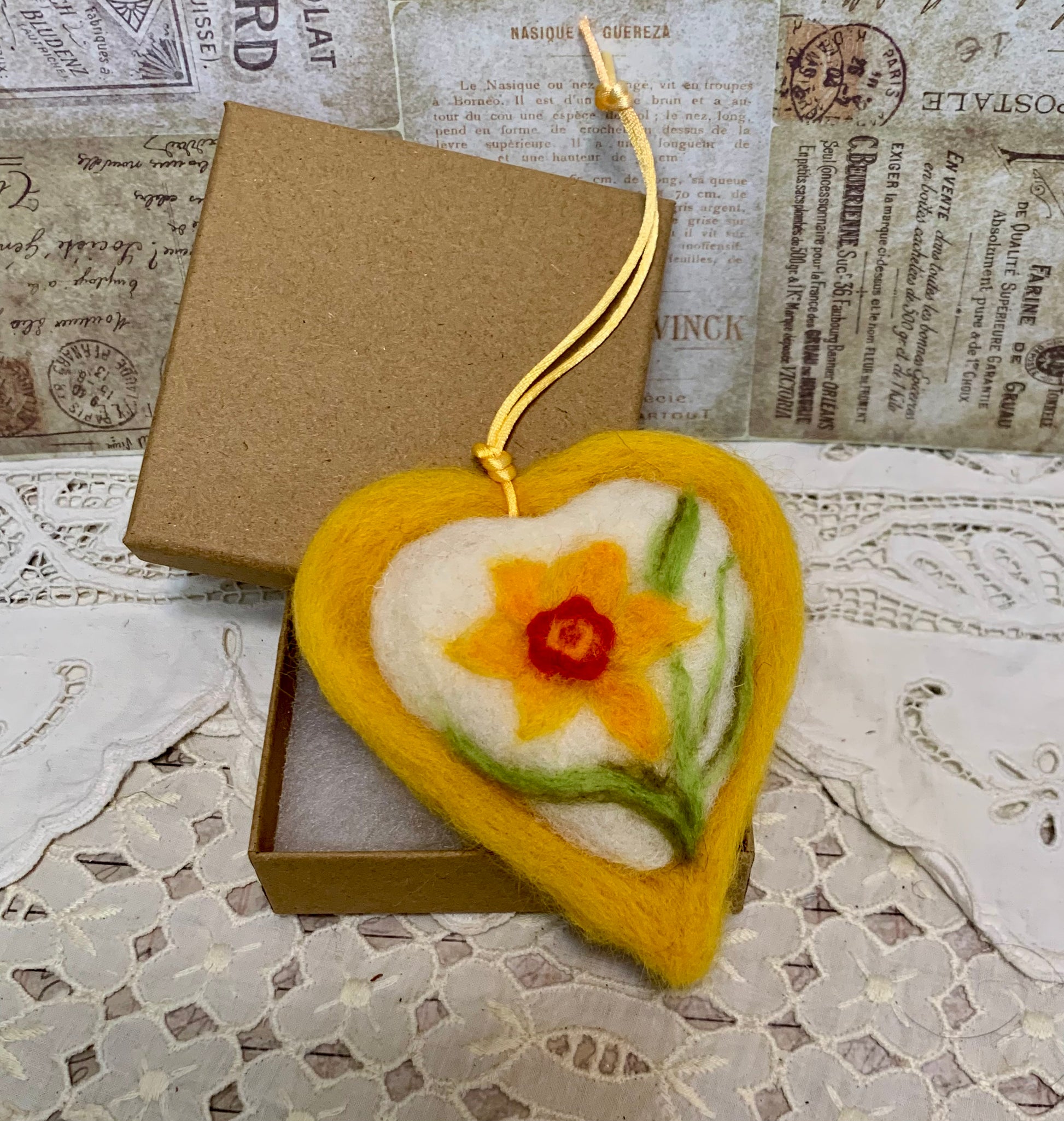 Heart-shaped felt ornament with a floral design in a box on a textured surface