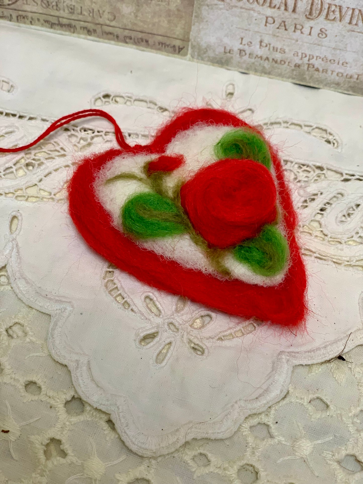 Heart-shaped felted ornament with a red rose on a lace background
