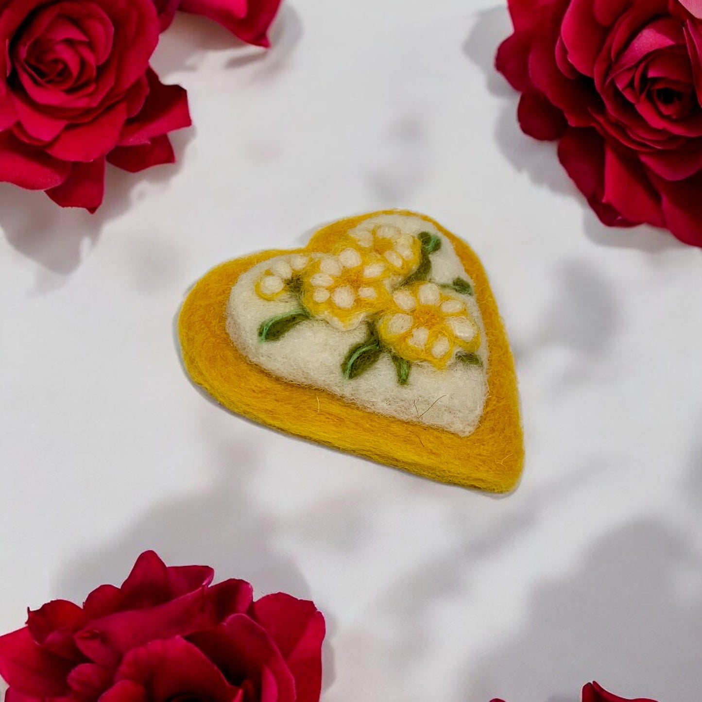 Heart-shaped embroidered patch with floral design on a white background surrounded by red roses.