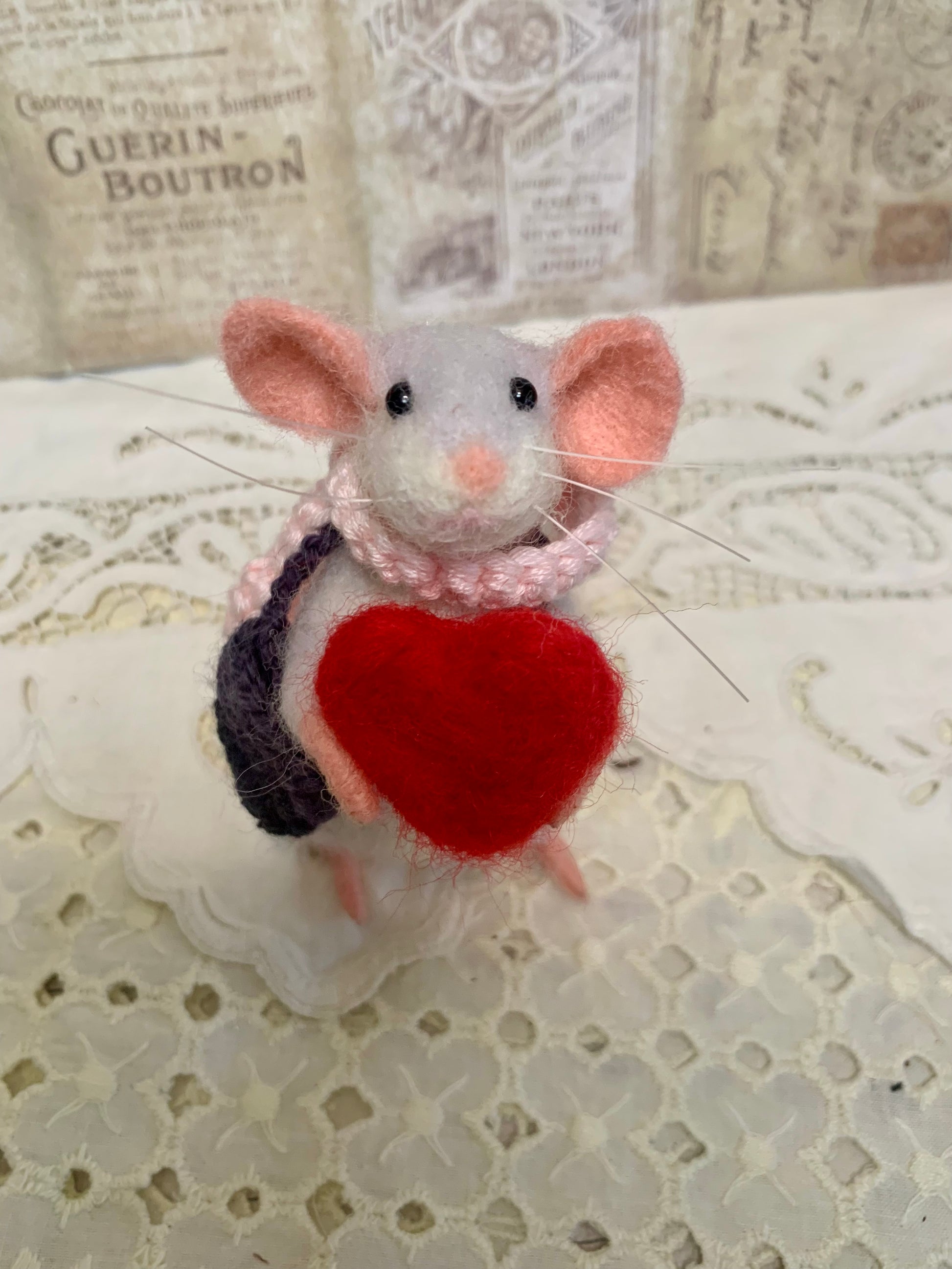 Stuffed mouse toy with a red heart on a lace background
