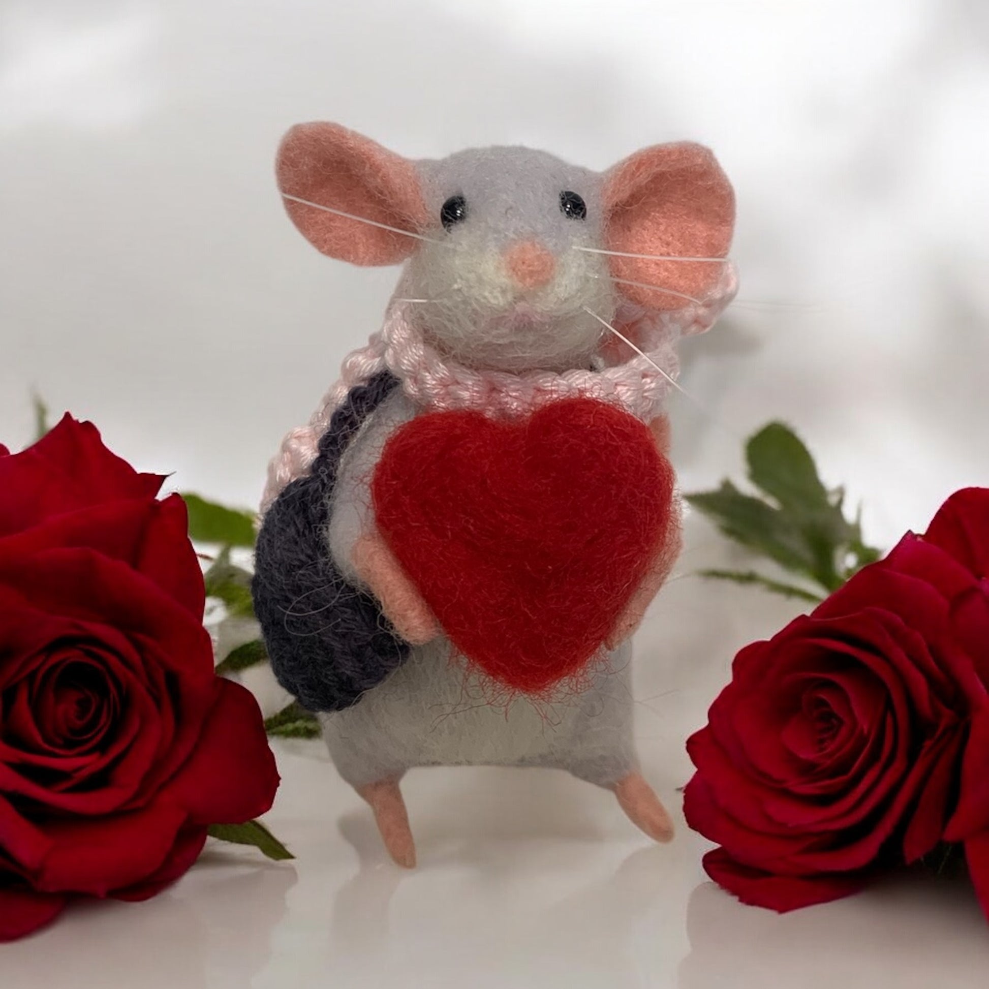Stuffed mouse toy with a red heart and backpack between two red roses on a white background