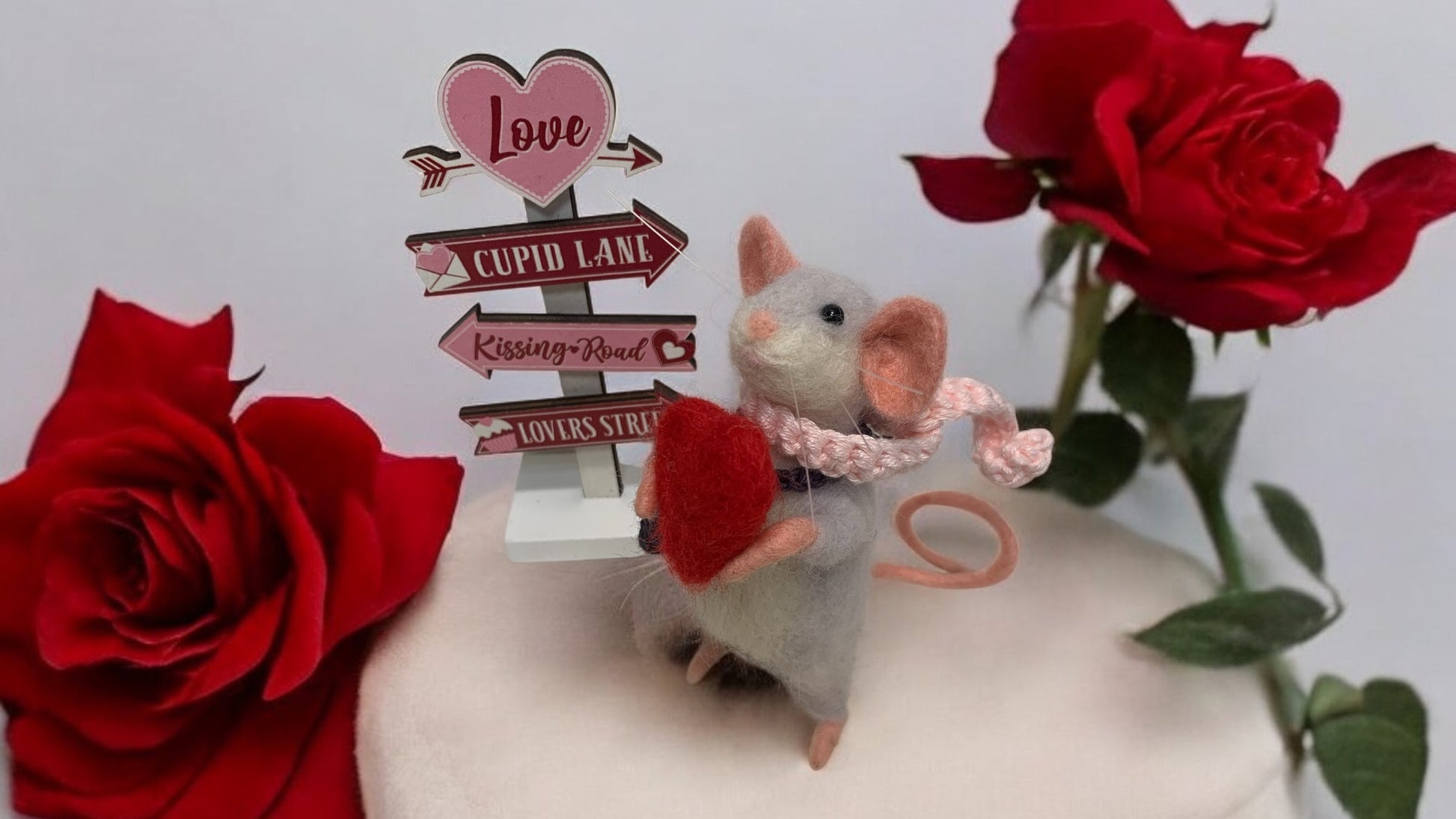 Small plush mouse with a heart, surrounded by red roses and decorative signs on a white background