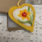 This handmade needle-felted heart is delicately embroidered with a yellow daffodil,